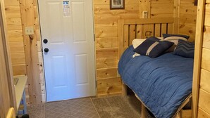 A wooden room with a bed, a door, and a small picture on the wall. - Cozy 2-bedroom cabin in adorable Tomahawk with AC (Tomahawk)