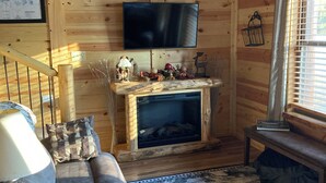 A cozy cabin interior with a fireplace, wooden walls, a television mounted above it, a sofa, and a patterned rug. - Cozy 2-bedroom cabin in adorable Tomahawk with AC (Tomahawk)