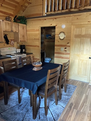 Een houten interieur met een eettafel, stoelen, een fornuis en een klok aan de muur.