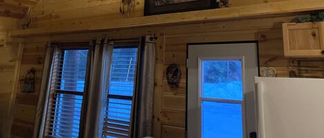 Un interior de madera con un ventilador de techo, dos ventanas con persianas, una puerta y un refrigerador.