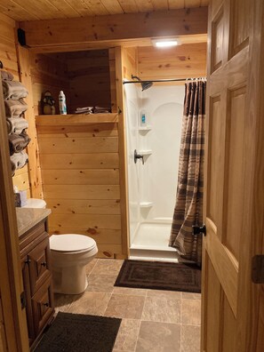 Een houten badkamer in een vakantiehuisje, met een toilet, douche en houten kastjes.