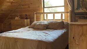 Ett sovrum i en stuga med träpanel, inrett med en enkelsäng, en byrå och ett fönster med gardiner.