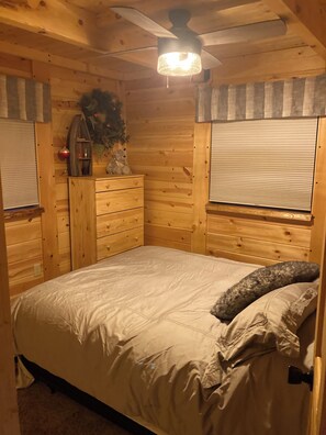 A wooden cabin bedroom with a bed, a dresser, a ceiling fan, and a window with blinds. - Cozy 2-bedroom cabin in adorable Tomahawk with AC (Tomahawk)