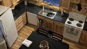 A compact kitchen with wooden cabinets, a black countertop, a white stove, and a dining area with a table and chairs. - Cozy 2-bedroom cabin in adorable Tomahawk with AC (Tomahawk)