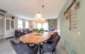 A dining area with a round wooden table, grey upholstered chairs, a hanging woven light fixture, and a television on a stand. - Pet friendly home in Wemeldinge with sauna (Wemeldinge)