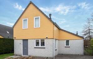 A two-story house with a yellow facade and white brick base, featuring a grey door and two windows on the upper floor. - Pet friendly home in Wemeldinge with sauna (Wemeldinge)