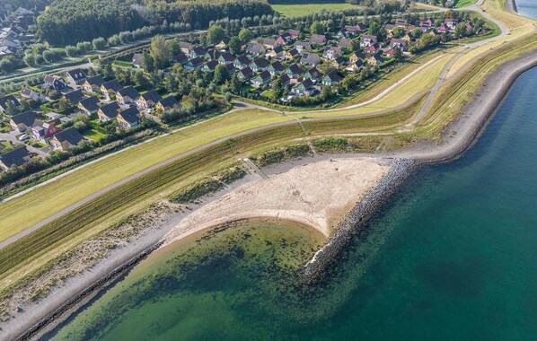 Vue aérienne d’une zone résidentielle côtière, avec des maisons, une plage et une étendue d’eau claire.