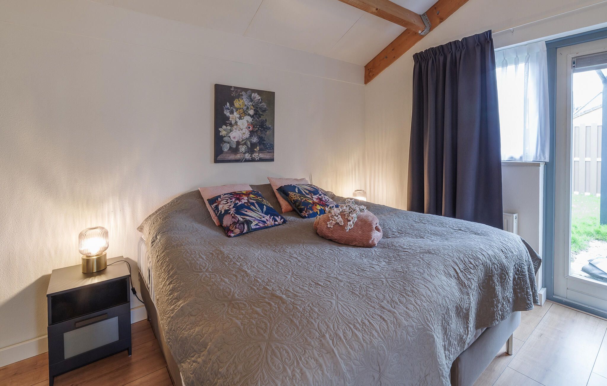 Una camera da letto con un letto, cuscini, un comodino, una lampada e un quadro appeso al muro.