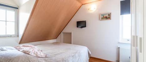 Une chambre avec un plafond en pente, un lit recouvert d’une courtepointe, un téléviseur fixé au mur et un radiateur.