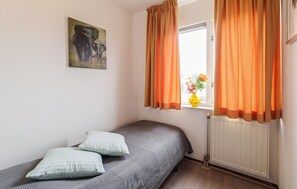 A bedroom with a single bed, two pillows, a window with orange curtains, a radiator, and a painting on the wall. - 3 bedroom lovely home in Wemeldinge (Wemeldinge)