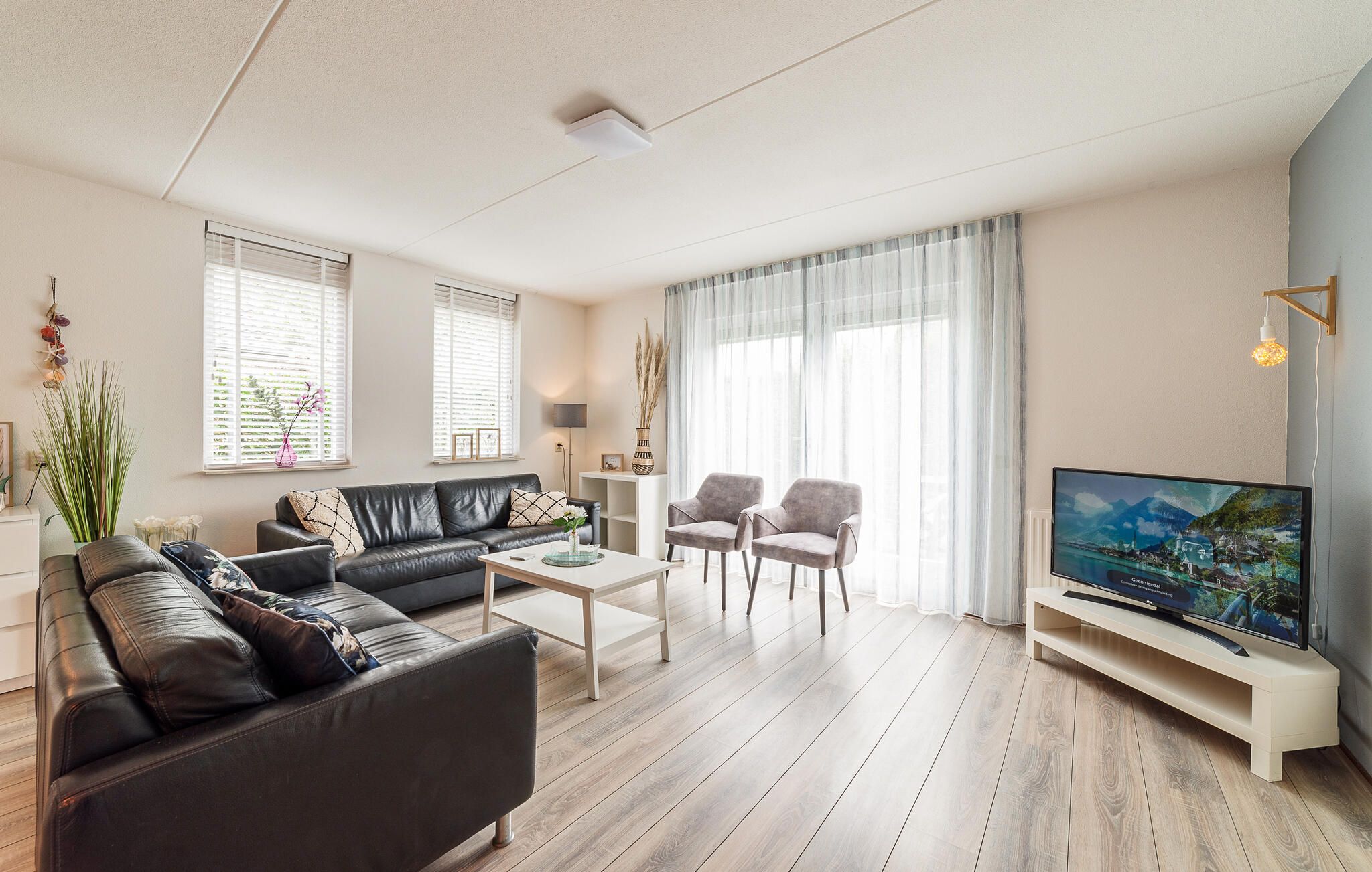 A modern living room with a leather sofa, two armchairs, a coffee table, and a flat-screen TV.