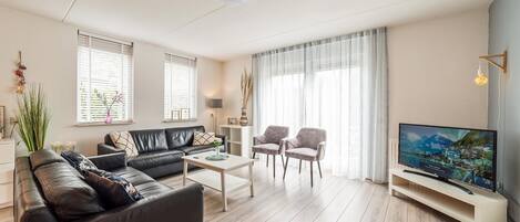 A modern living room with a leather sofa, two armchairs, a coffee table, and a flat-screen TV.