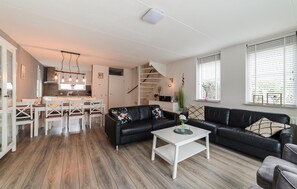 A modern living space with a dining area, a black leather sofa, and a staircase leading to an upper level. - Gorgeous home in Wemeldinge with sauna (Wemeldinge)
