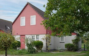 Ein rotes und graues Haus mit zwei Fenstern, umgeben von viel Grün.