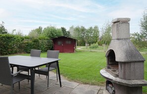 Eine Terrasse mit einem gemauerten Außenofen, einem roten Holzschuppen und einem Tisch mit Stühlen.