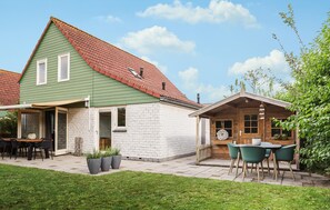 A two-story house with a green roof, a patio with outdoor seating, and a small wooden structure with a door. - Awesome home in Wemeldinge with sauna (Wemeldinge)