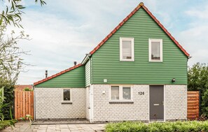 A two-story house with a green roof and white brick walls, featuring a front door and two windows. - Awesome home in Wemeldinge with sauna (Wemeldinge)