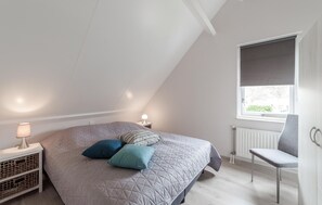 A bedroom with a sloped ceiling, a bed with a quilted cover, two bedside lamps, a window with a blind, and a chair. - Nice home in Wemeldinge with WiFi (Wemeldinge)