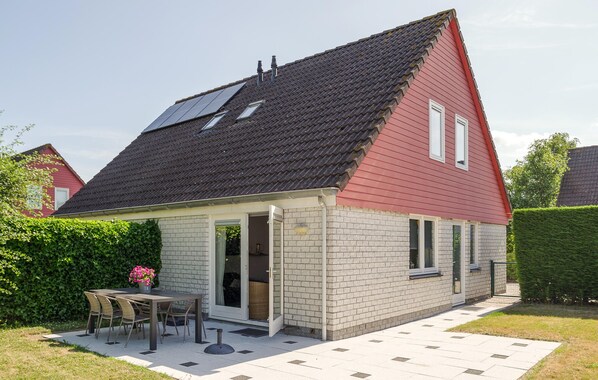 A single-story house with a red exterior, a tiled roof, and a small patio area with a table and chairs. - Nice home in Wemeldinge with WiFi (Wemeldinge)