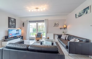 Ein modernes Wohnzimmer mit Ledersofa, Glastisch, Flachbildfernseher und einer großen Glasschiebetür, die auf einen Balkon führt.