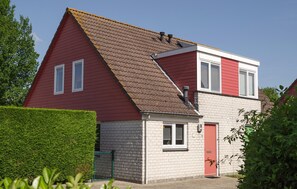 Ein zweistöckiges Haus mit roter Fassade, einem Klinkerunterbau und einem geneigten Dach.