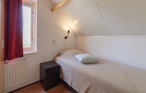 A bedroom with a bed, a nightstand, a wall-mounted light, a window with curtains, and a radiator. - Awesome home in Wemeldinge with sauna (Wemeldinge)