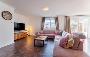 A modern living room with a flat-screen TV, wooden cabinet, and a large pink sofa.