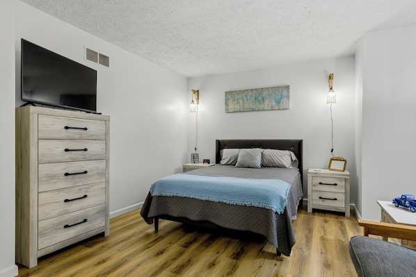 A bedroom with a bed, a dresser, a television, bedside lamps, and a painting on the wall.