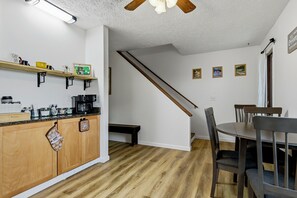 A modern kitchen with wooden cabinets, a coffee station, and a dining area with a table and chairs.