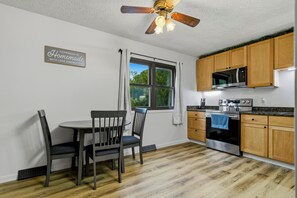 A kitchen with wooden cabinets, a microwave, an oven, a ceiling fan, and a dining table with chairs.