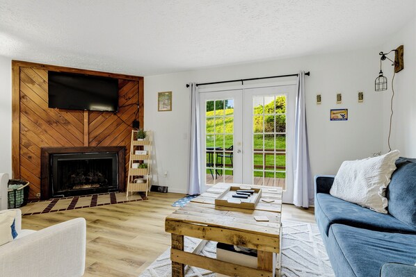 A living room with a fireplace, a television mounted on the wall, and a view through the glass doors to the outside.