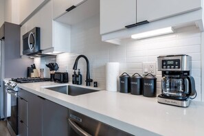 Ett modernt kök med en spis i rostfritt stål, en kaffebryggare och tre märkta behållare för te, kaffe och socker.