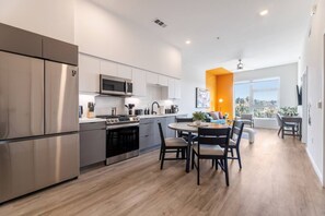 A modern kitchen with stainless steel appliances, a dining area with a round table, and a bright orange accent wall.