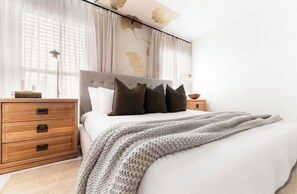 A neatly made bed with a grey knitted blanket, a wooden nightstand with a lamp, and a bedside table with a book. - The Wild Tumbleweed/ 3-bedroom house in quaint Lubbock- Best of the West (Lubbock)