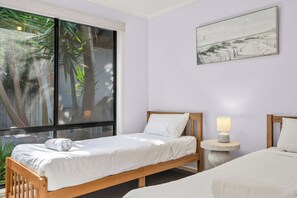 Een hotelkamer met twee bedden, een raam met uitzicht op palmbomen en een schilderij aan de muur.