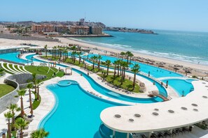 Ein Resort mit einem großen, geschwungenen Pool, Palmen und Blick auf den Strand.