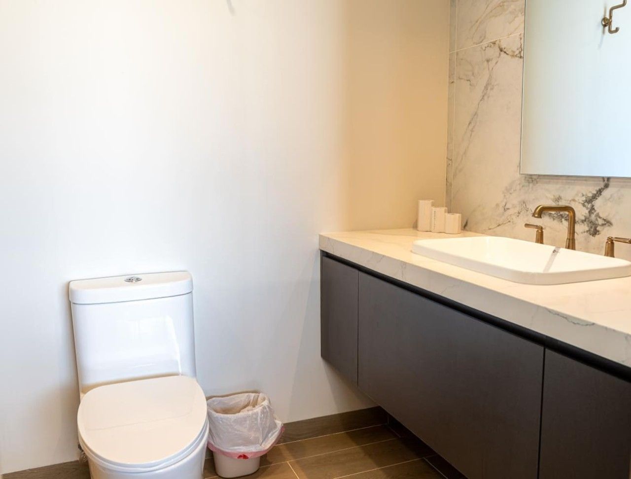 A bathroom with a toilet, sink, and marble backsplash.