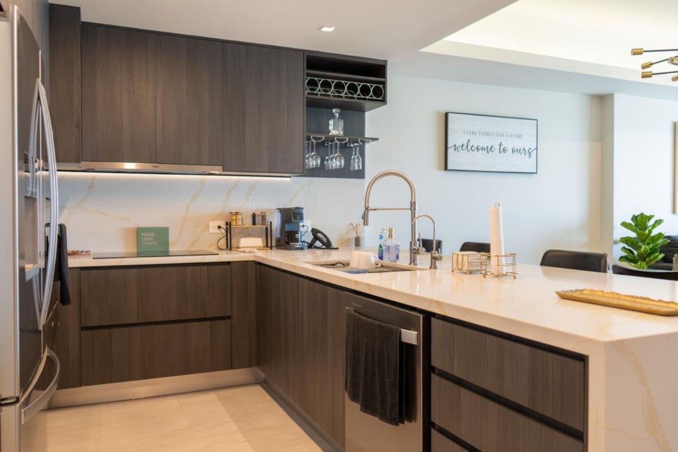 A modern kitchen with dark wood cabinets, a white countertop, a built-in wine rack, and a kitchen island with a sink and bar tools.