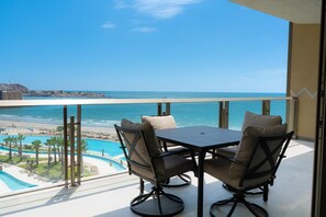 Ein Balkon mit Tisch und Stühlen mit Blick auf einen Pool und Strand.