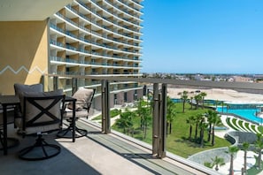 A balcony with a view of a hotel building, a pool, and a beach. - Sonoran Star Beachfront 2BR - Ocean & Pool Views · Jacuzzi · Beach Access (Puerto Peñasco)