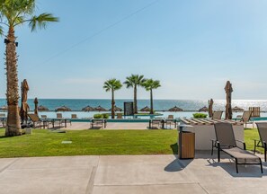 Un área junto a la piscina con sillones, palmeras y vista al océano.