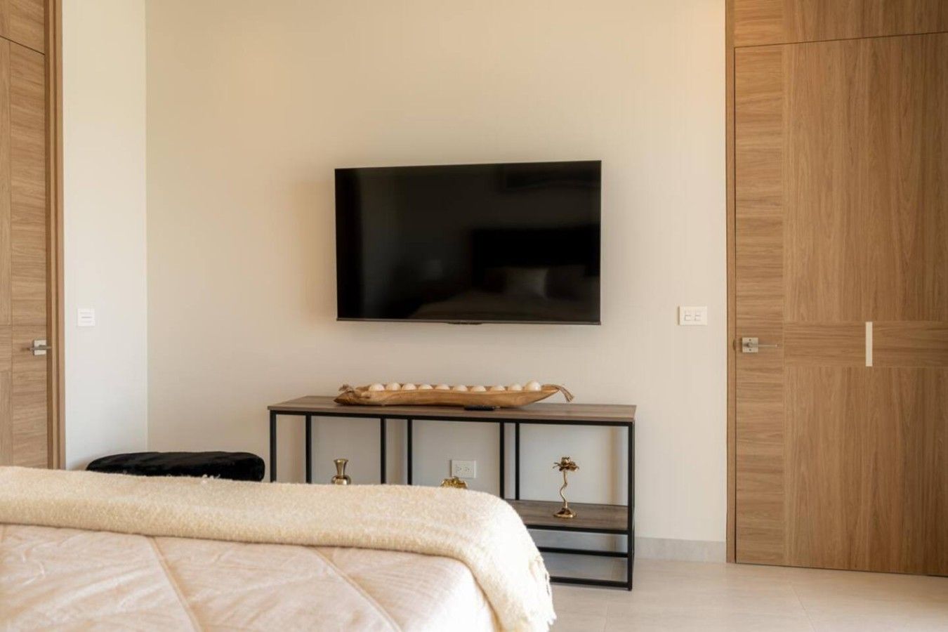 Une chambre à coucher comprenant un lit, un téléviseur fixé au mur, une table de chevet agrémentée d’objets décoratifs et une armoire.