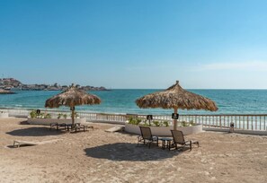 Un espace aménagé au bord de la plage, avec des parasols en chaume, des chaises longues et une vue sur la mer.