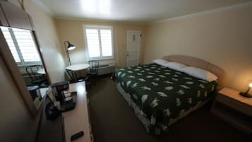 A hotel room with a bed, a desk with a chair, a desk lamp, a coffee maker, and a window with blinds.