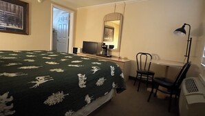 Hotellihuone, jossa on sänky, työpöytä, tietokone, tuoli, pöytälamppu ja peili.