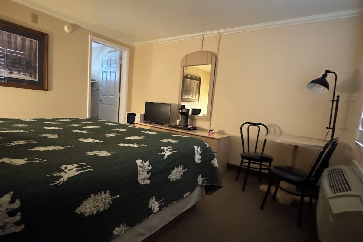 Een hotelkamer met een bed, een bureau met een computer, een stoel, een bureaulamp en een spiegel.