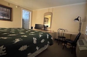 Een hotelkamer met een bed, een bureau met een computer, een stoel, een bureaulamp en een spiegel.