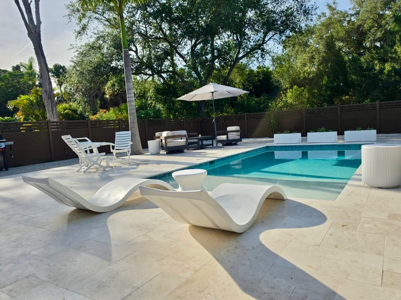 A modern outdoor pool area with white lounge chairs and a pool table.