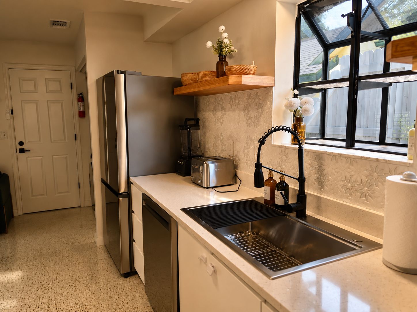 A compact kitchen with a refrigerator, toaster, blender, and a sink with a faucet.