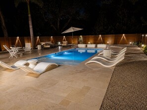A swimming pool with lounge chairs and a wooden deck at night. - Sarasota Slice of Paradise (Sarasota)